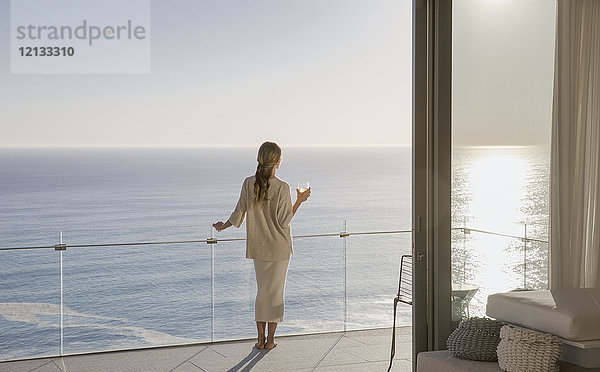 Frau auf sonnigem Luxusbalkon mit Meerblick stehend