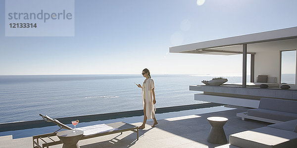 Frau  die auf der sonnigen  modernen  luxuriösen Musterhaus-Terrasse mit Meerblick spazieren geht