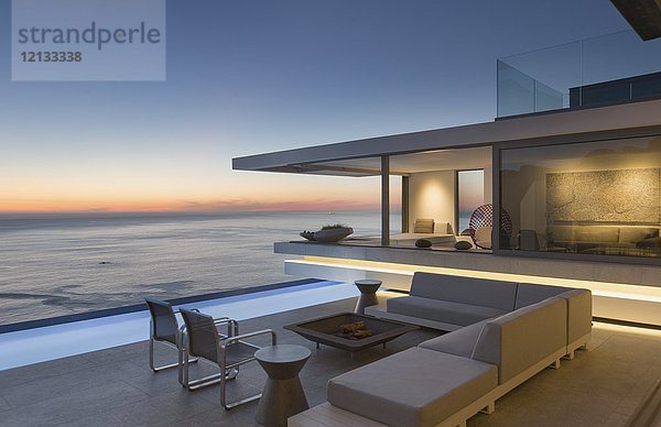 Beleuchtete  moderne Luxuswohnung mit Außenterrasse  Sofa und Pool mit Meerblick in der Abenddämmerung