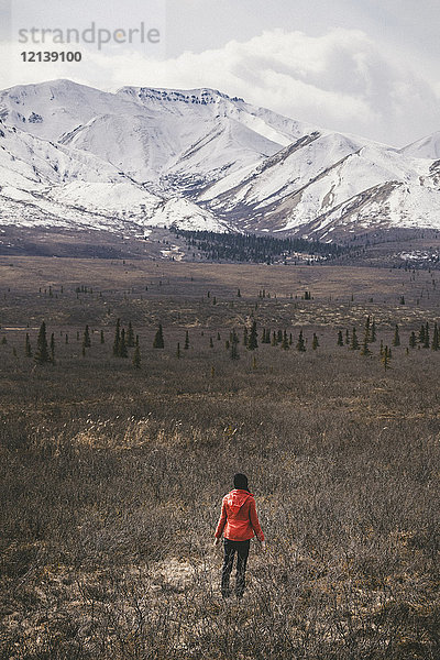 Kaukasische Frau steht auf einem Feld in der Nähe eines verschneiten Berges