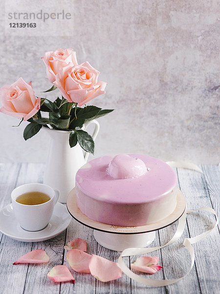 Rosa Kuchen mit Tee in der Nähe Vase mit Blumen