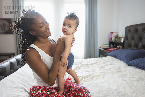 Mutter sitzt auf dem Bett und hält ihre kleine Tochter