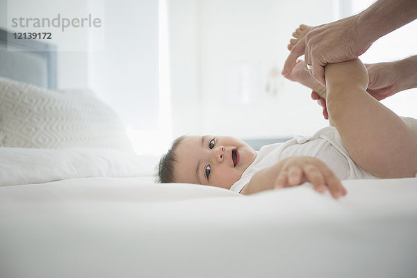 Vater hält die Beine seines kleinen Sohnes auf dem Bett