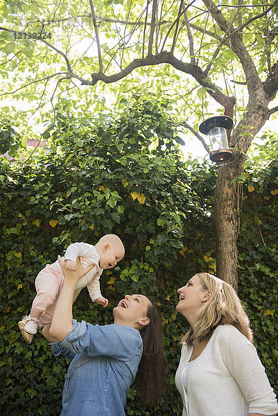 Kaukasische Mütter heben ihre kleine Tochter unter den Baum