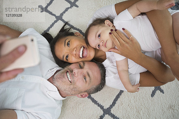 Familie liegt auf dem Boden und posiert für ein Selfie mit dem Handy