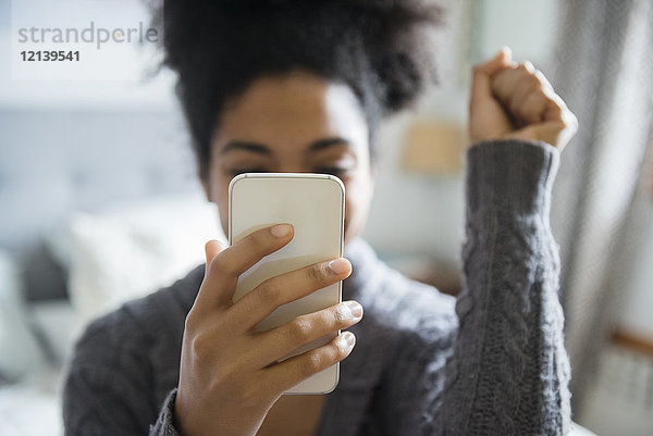 Afroamerikanische Frau feiert  während sie eine SMS auf ihrem Handy schreibt