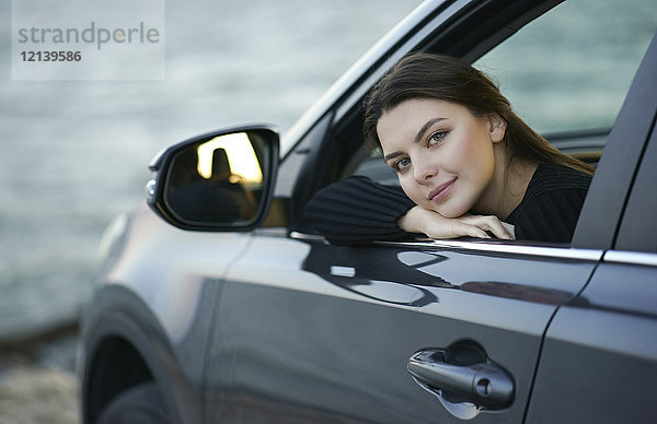 Lächelnde kaukasische Frau lehnt sich ins Autofenster