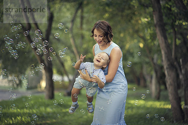 Kaukasische Mutter hält ihren kleinen Sohn und spielt mit Seifenblasen