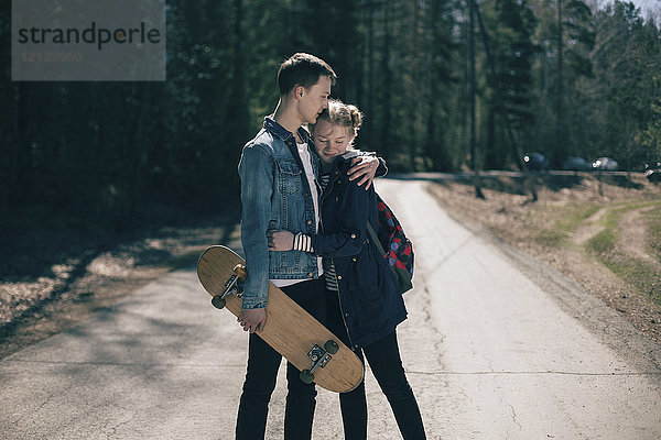 Kaukasisches Paar mit Skateboard  das sich auf der Straße umarmt
