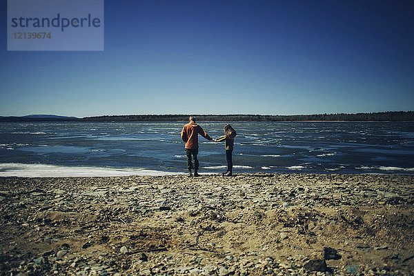 Entferntes kaukasisches Paar hält Hände am Strand