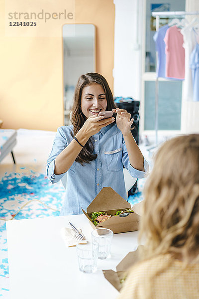 Fröhliche junge Frau beim Fotografieren des Takeaway-Salats auf dem Tisch