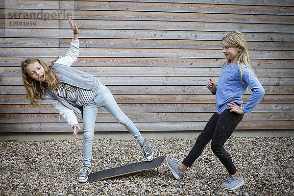 Zwei Mädchen mit Skateboard vor einer Holzfassade