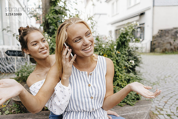 Zwei glückliche junge Frauen mit Handy in der Stadt