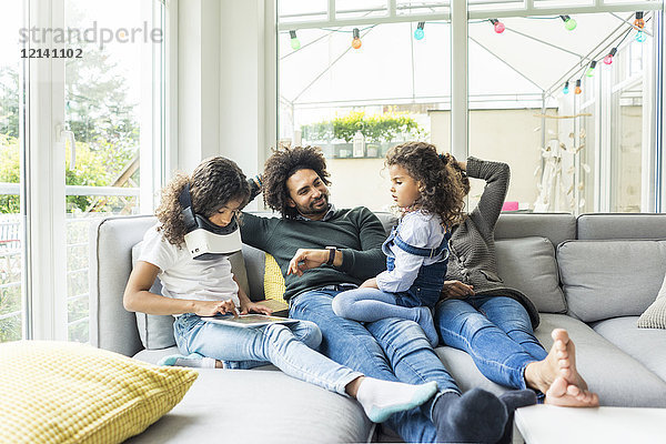 Glückliche Familie sitzt auf der Couch  Tochter spielt mit digitalem Tablett