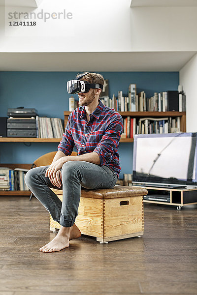Junger Mann zu Hause sitzend auf Box mit VR-Brille
