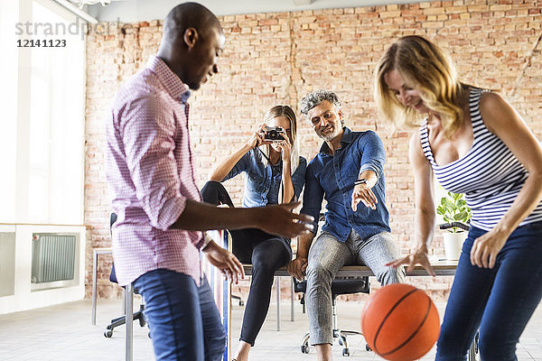 Frau fotografiert Kollegen beim Basketballspielen im Büro