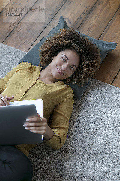 Lächelnde junge Frau zu Hause auf dem Boden liegend mit Laptop