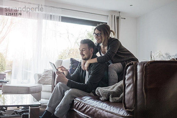 Lächelndes Paar sitzt auf der Couch zu Hause mit Tablette