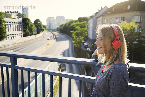 Porträt einer lächelnden jungen Frau beim Musikhören mit Kopfhörern