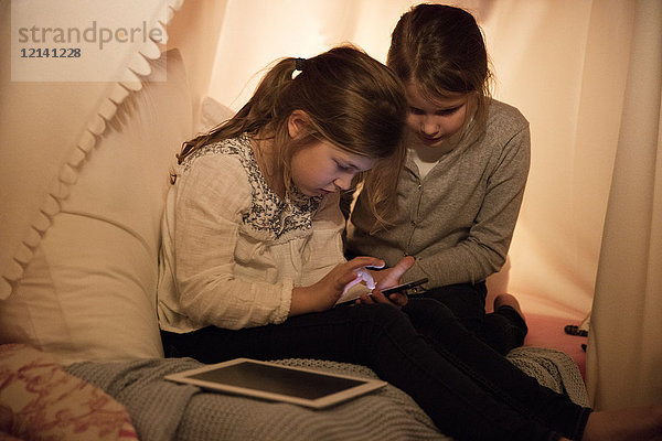 Zwei Mädchen mit Handy und Tablette im Kinderzimmer