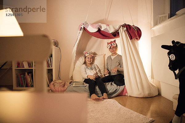 Portrait von zwei glücklichen Mädchen mit Tablette im Kinderzimmer