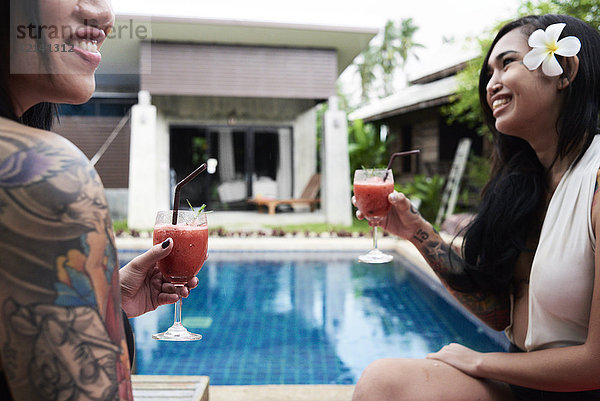Zwei fröhliche Frauen trinken Cocktails im Schwimmbad