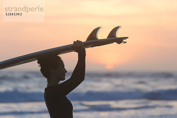 Indonesien  Bali  junge Frau mit Surfbrett am Kopf bei Sonnenuntergang