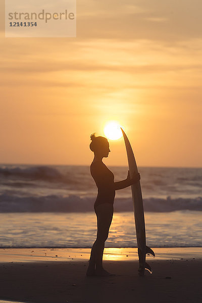 Indonesien  Bali  junge Frau mit Surfbrett bei Sonnenuntergang