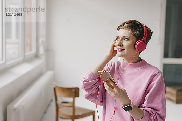 Lächelnde Frau mit Handy und Kopfhörer beim Musikhören
