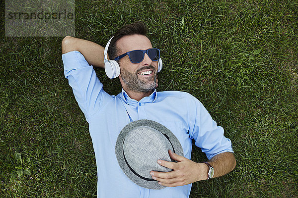 Porträt eines lachenden Mannes  der sich auf einer Wiese entspannt und Musik mit Kopfhörern hört  Draufsicht