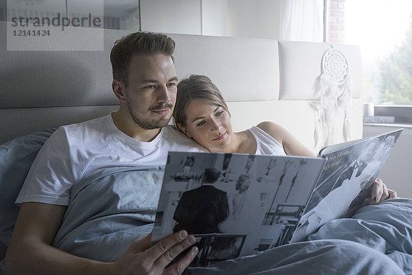 Paar im Bett zu Hause beim Betrachten des Hochzeitskatalogs