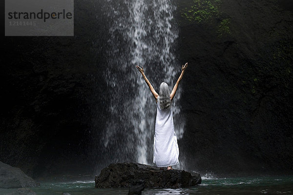 Schöne Seniorin vor einem tropischen Wasserfall stehend
