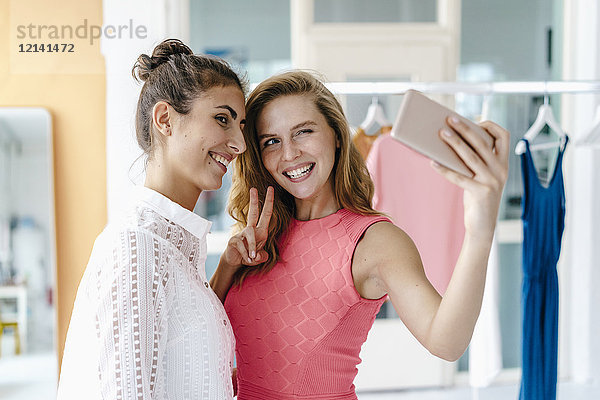 Zwei lächelnde junge Frauen  die einen Selfie im Modestudio nehmen.