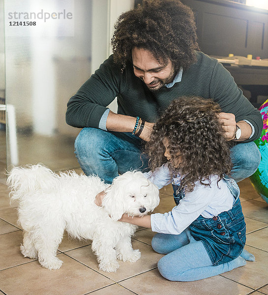 Vater und Tochter spielen mit einem kleinen Hund zu Hause