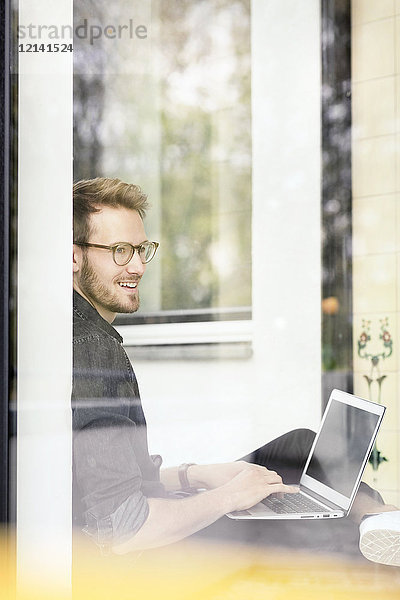 Porträt eines lächelnden Mannes mit Laptop am Fenster