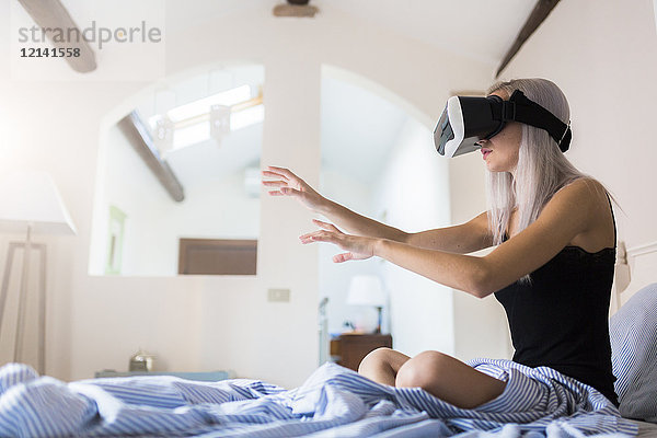 Junge Frau im Bett sitzend mit VR-Brille