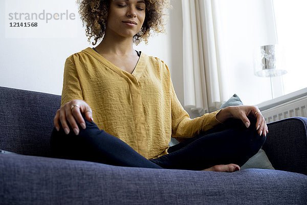 Junge Frau sitzt zu Hause auf der Couch und meditiert.