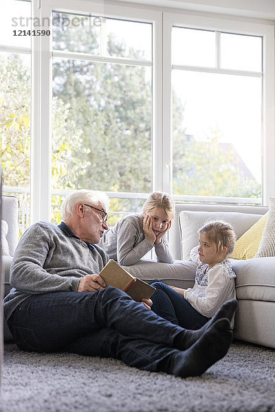 Zwei Mädchen und Großvater beim Lesen im Wohnzimmer