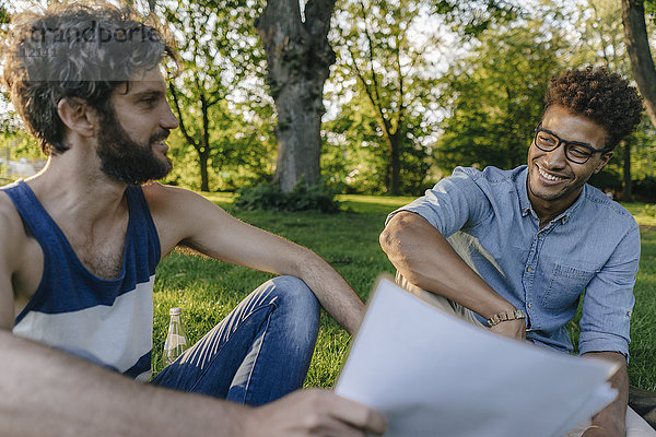 Zwei Freunde  die in einem Park sitzen und über Papiere diskutieren.