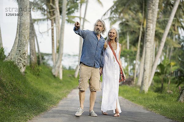 Hübsches Seniorenpaar beim Spaziergang durch tropische Landschaft mit Palmen