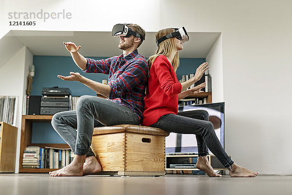 Junges Paar zu Hause auf Box sitzend mit VR-Brille
