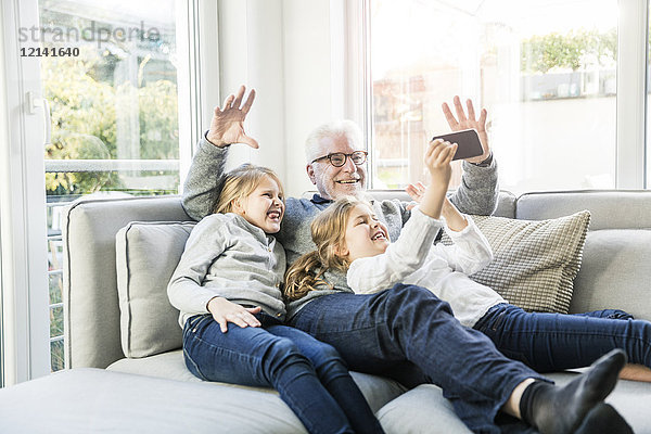 Zwei glückliche Mädchen und Großvater auf dem Sofa  die einen Selfie nehmen.