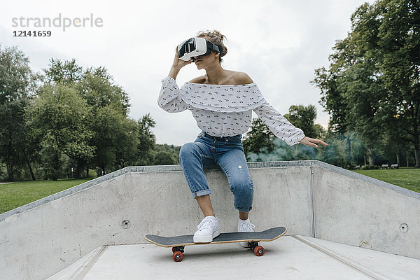 Junge Frau mit Skateboard mit VR-Brille im Skatepark
