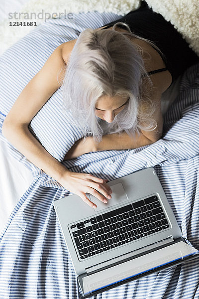Junge Frau im Bett liegend mit Laptop