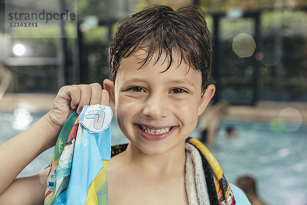 Porträt eines stolzen Jungen  der sein Schwimmabzeichen am Beckenrand eines Hallenbades zeigt.