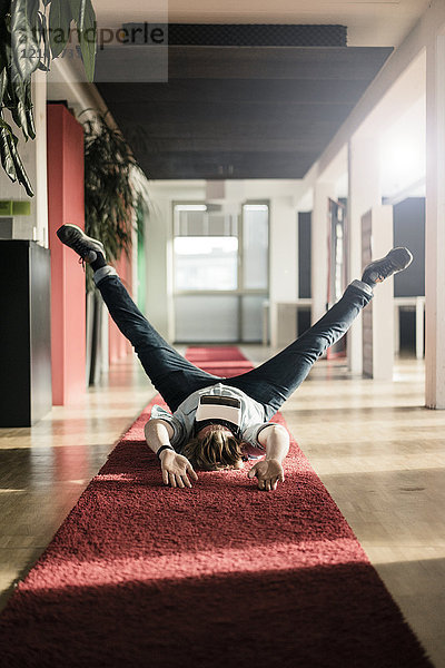 Geschäftsmann auf Teppichboden liegend mit VR-Brille beim Training