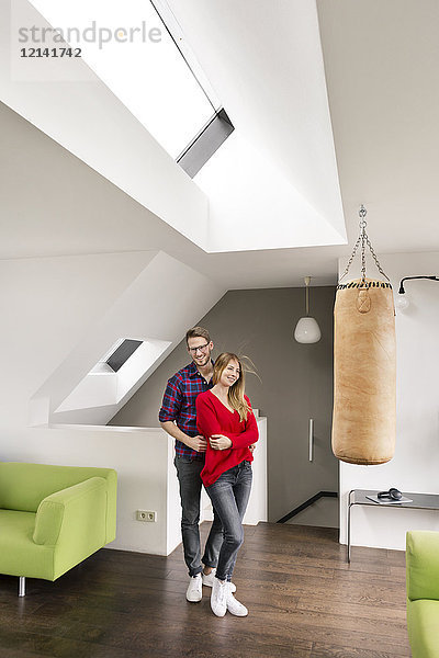 Porträt eines lächelnden jungen Paares  das zu Hause im Wohnzimmer steht.