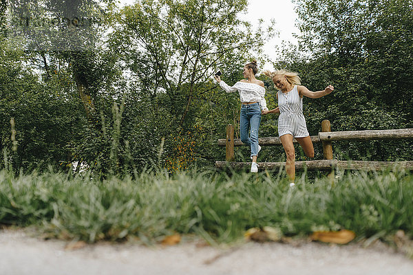 Zwei glückliche junge Frauen  die vom Zaun in einem Park springen.