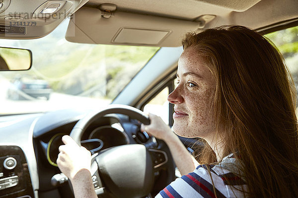 Lächelnde junge Frau mit Sommersprossen beim Autofahren  die zur Seite schaut