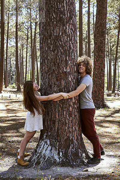 Glückliches junges Paar umarmt einen Baum im Wald